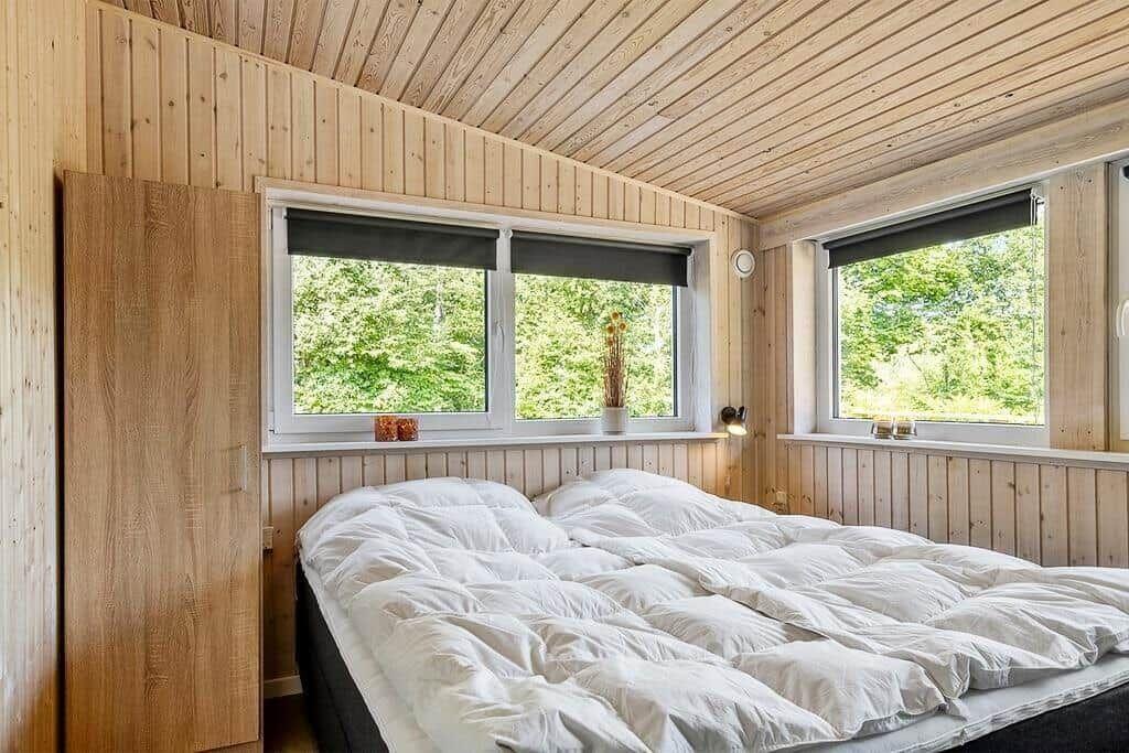 Bedroom with wooden walls, large bed, and windows with view of trees.