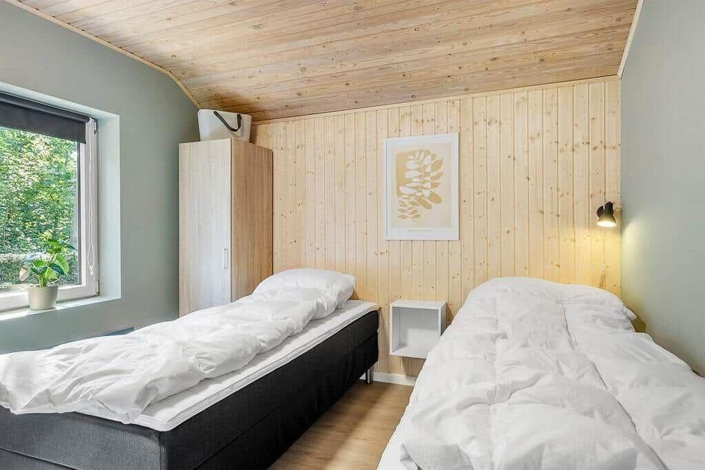 Two beds in a room with wooden wall and window.