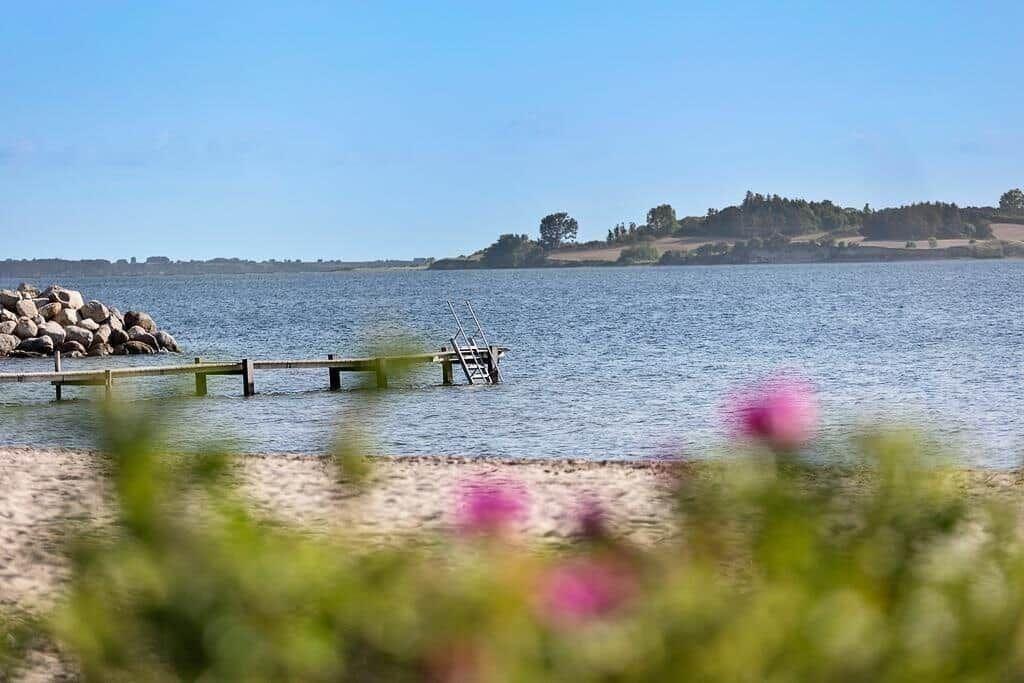 Lake shore with wooden pier and sandy beach. Hills with trees in the background.