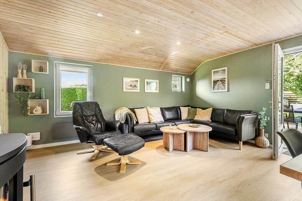 Living room with black leather sofa, wooden table and chair. Wooden ceiling and green walls.