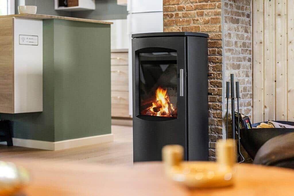 Black wood-burning stove with fire against stone wall.