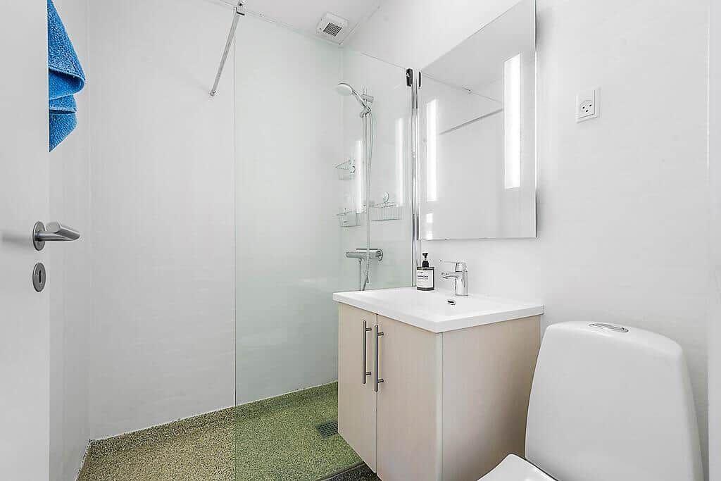 Shower with glass enclosure, sink and toilet in white finish.
