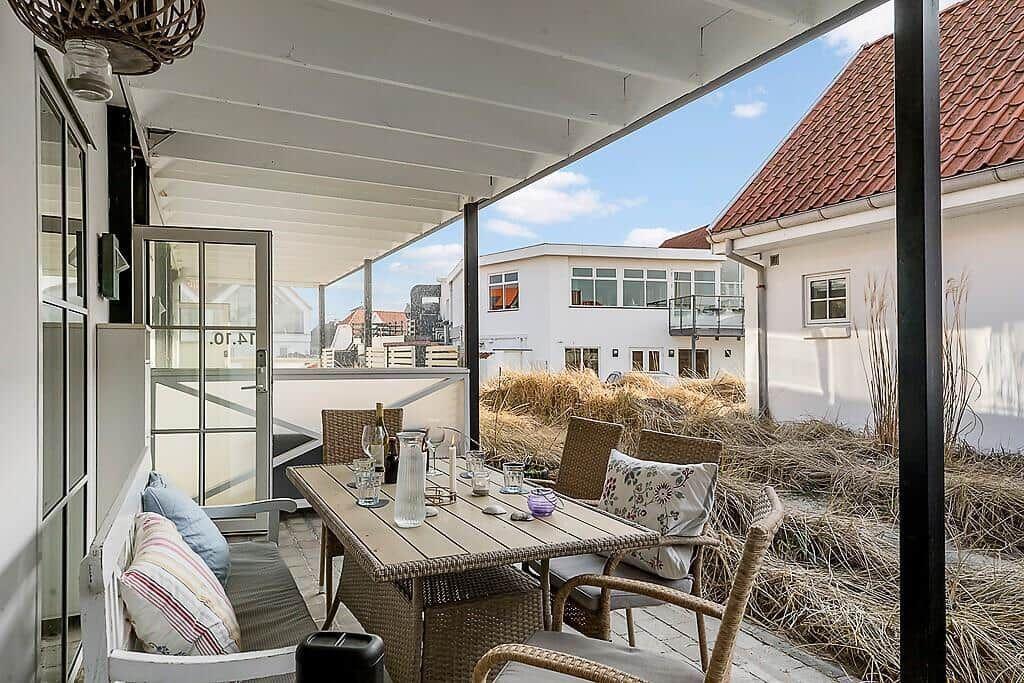 Terrace with table, chairs, and bench. View of white houses and grass.