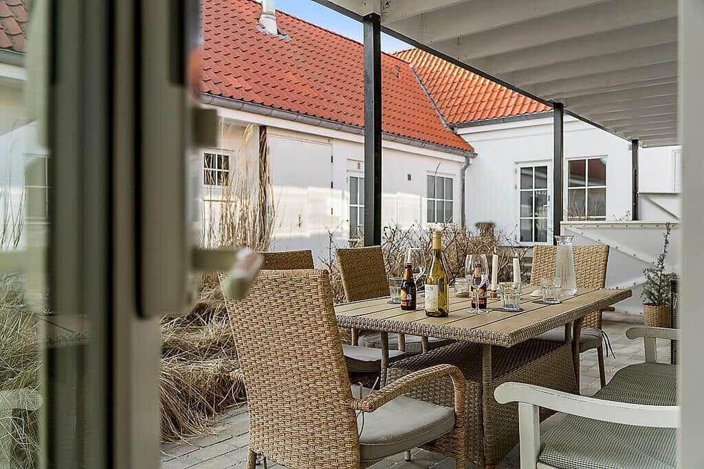 Terrace with dining table and chairs, view of white buildings with red roofs.