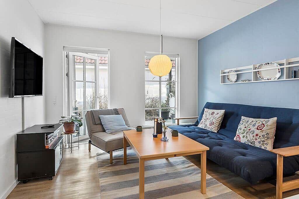 Living room with sofa, armchair, coffee table, and TV. Blue wall and windows to terrace.