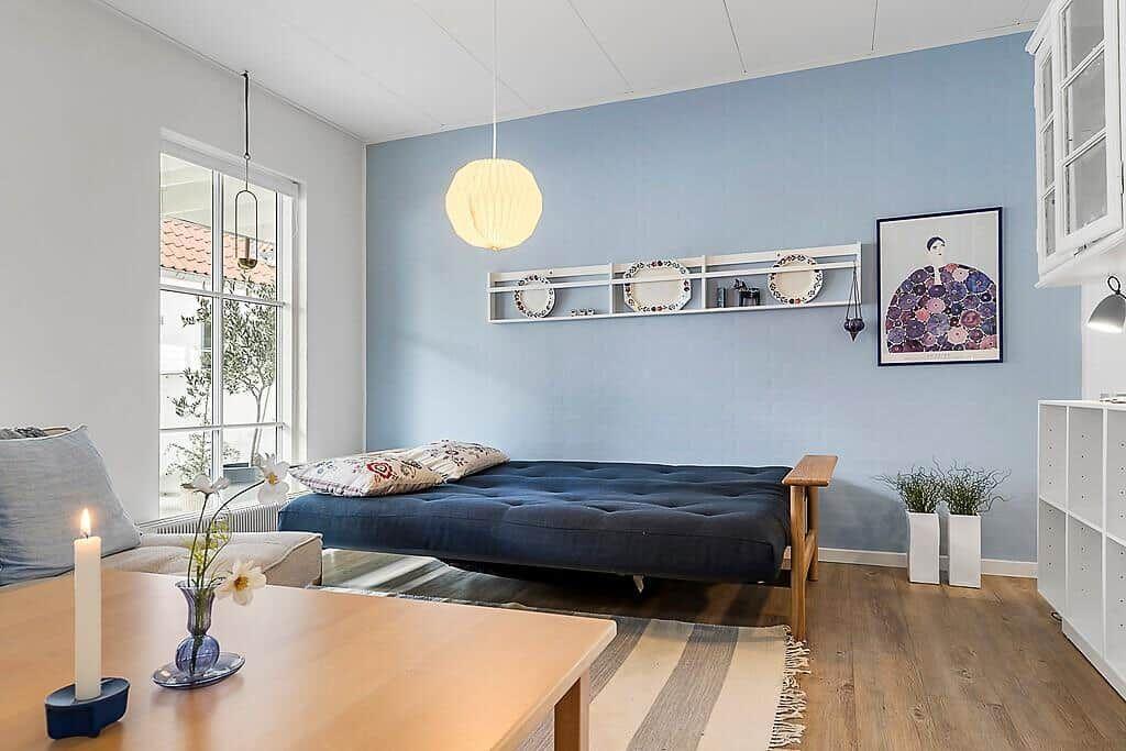 A room with blue wall, futon bed, table, and window.