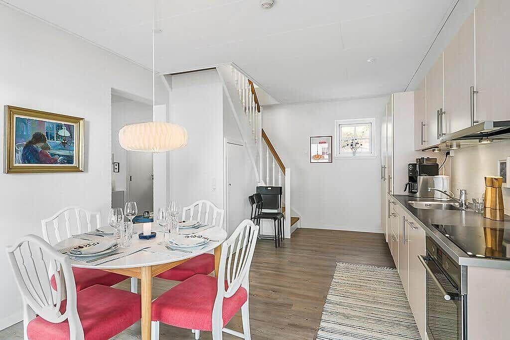 Dining area with table and chairs, kitchen and staircase in background.