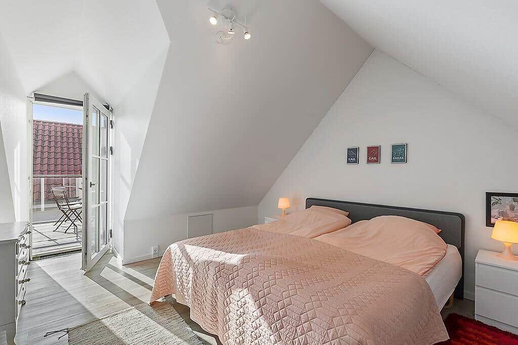 Bedroom with sloped ceiling, bed, and balcony access.