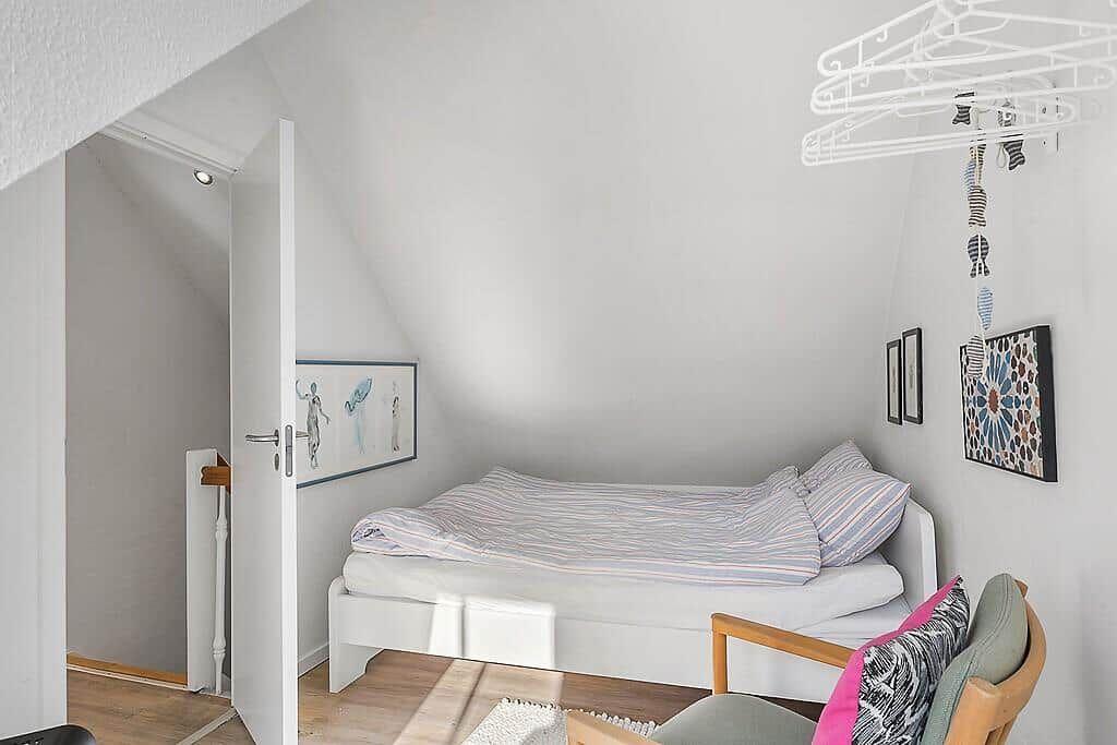 Bedroom with bed, chair, and wall art under sloped ceiling.