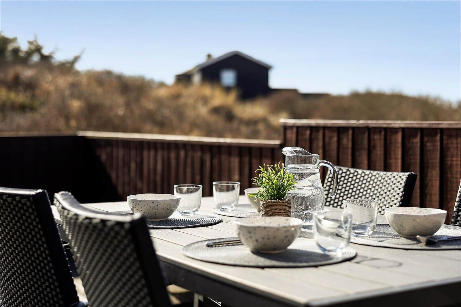 Covered balcony with table, chairs, and view of the house.