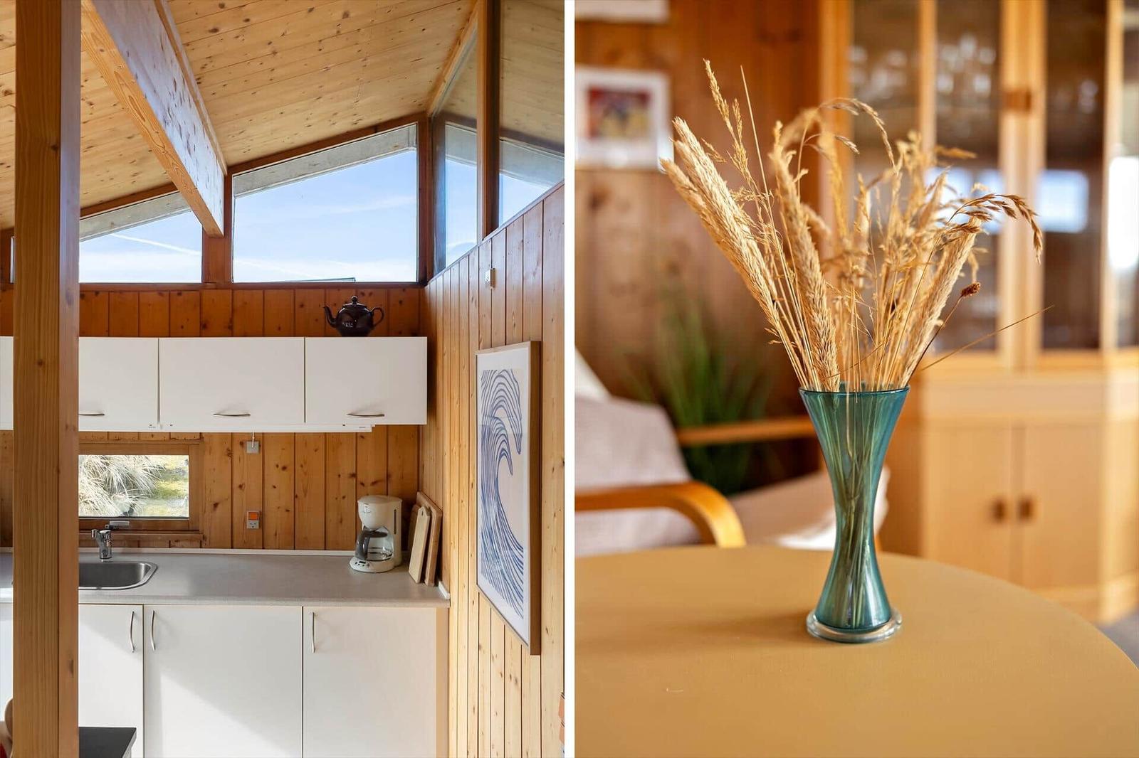 Kitchen with wooden walls and windows. Table with vase and dried grass.