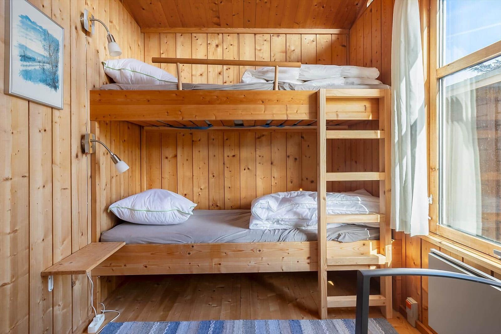 Bunk bed in a wood-paneled room with window and wall lamp.