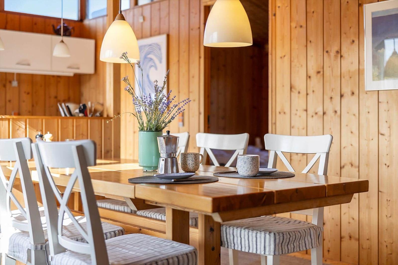 Dining room with wooden table, white chairs, and lavender flowers.