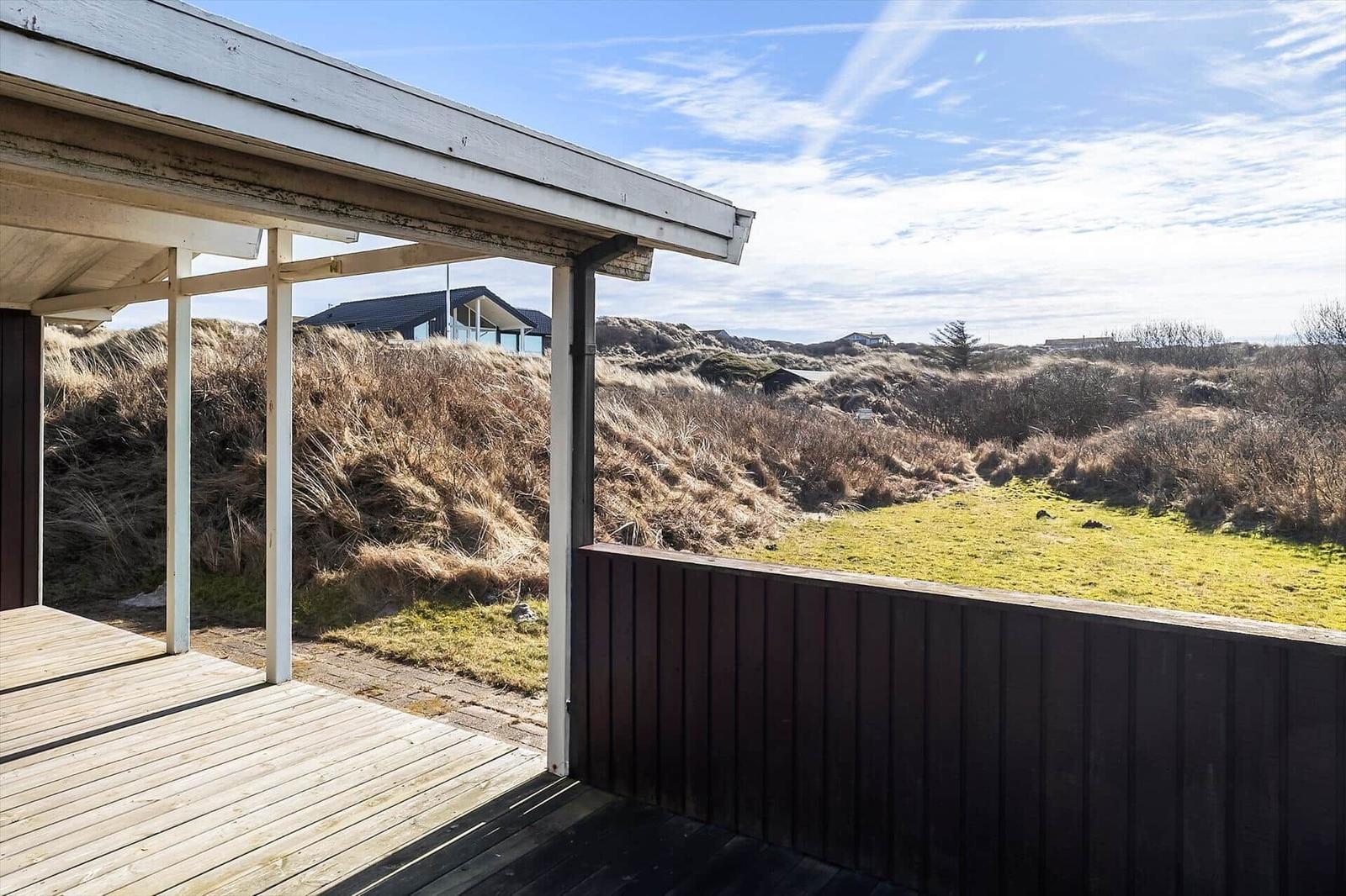 Deck with view of dunes and grassy areas under blue sky.