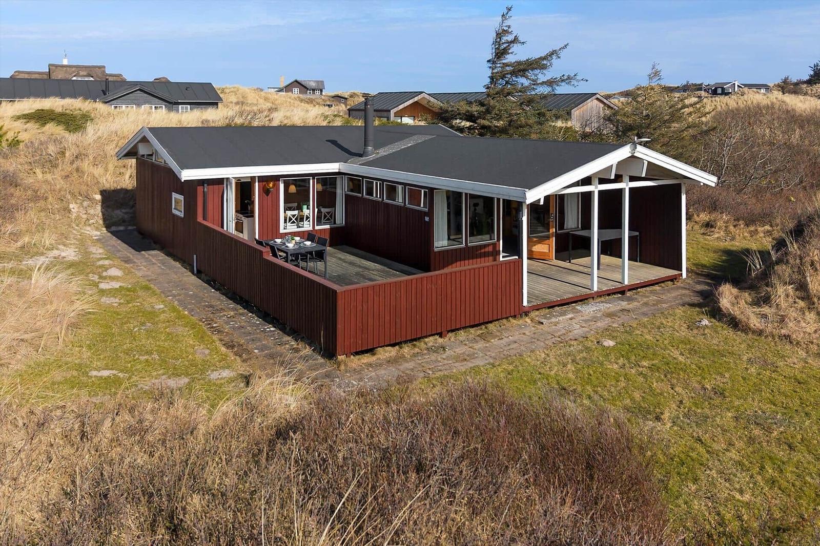 Red wooden house with terrace and garden. View of surrounding houses.