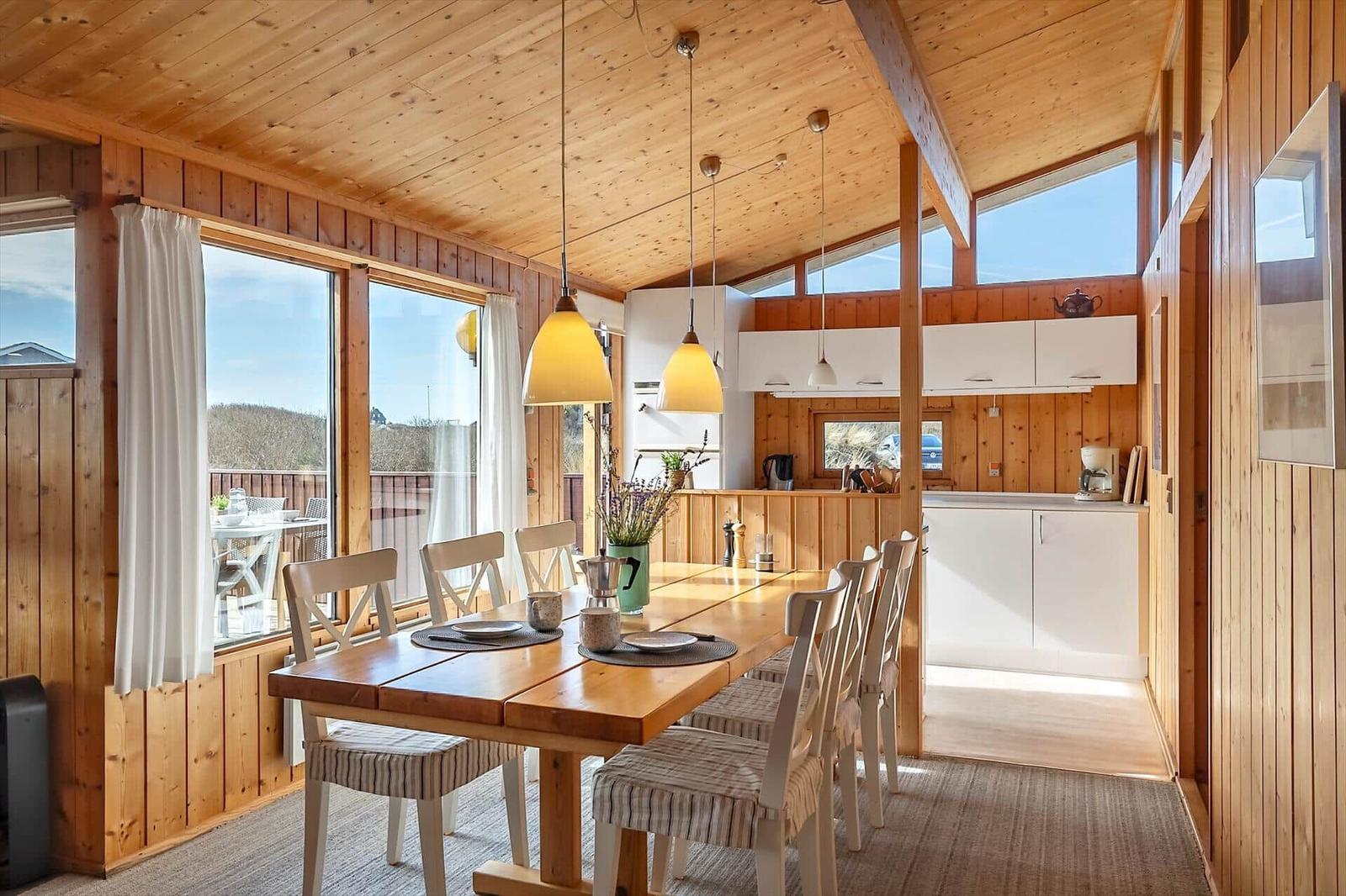 Dining room with wooden table, chairs, and kitchen area with white cabinets.
