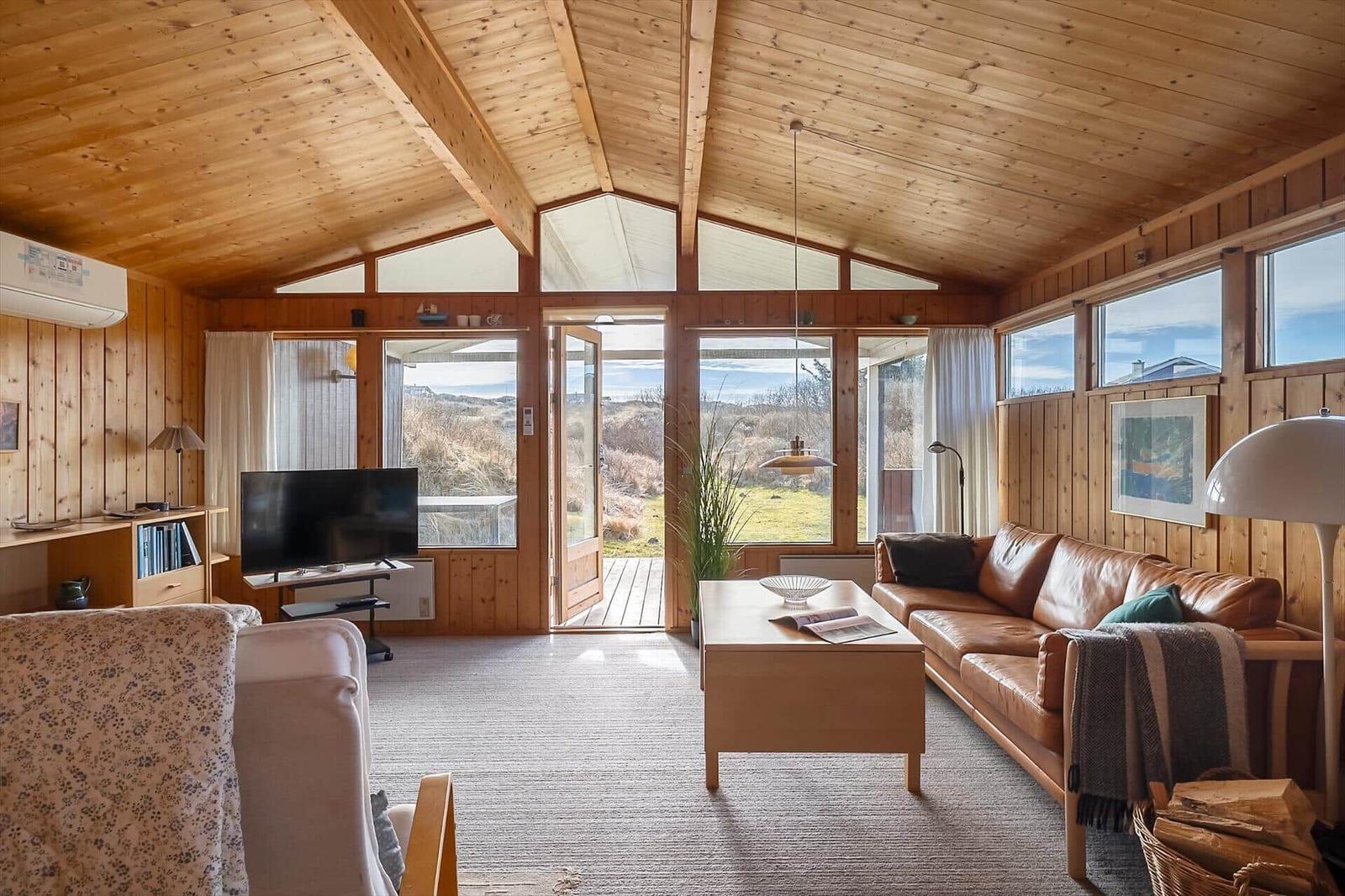 Living room with wooden walls, sofa, TV, and view of the landscape.