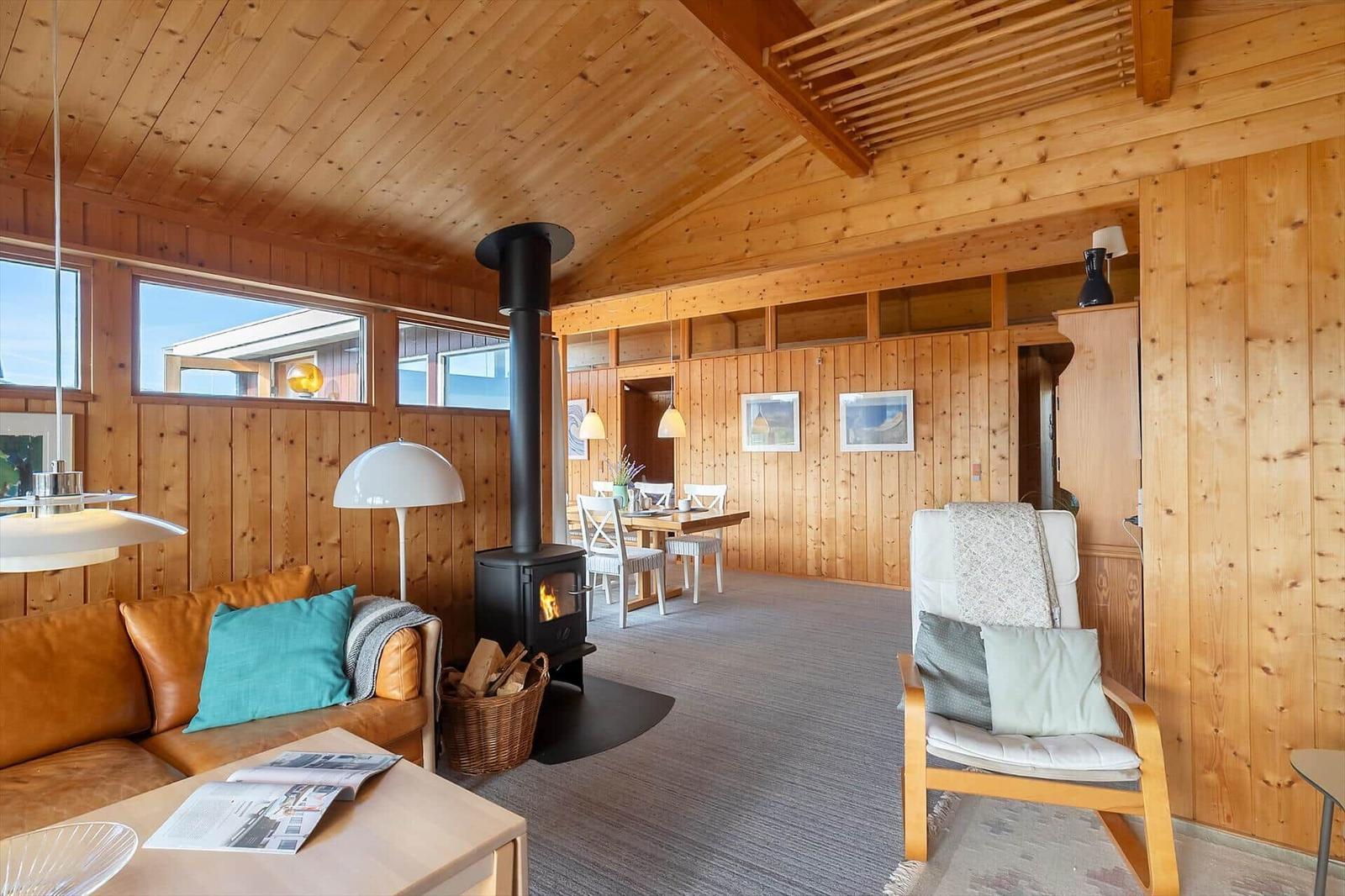 Living room with fireplace, sofa, and dining area. Wooden walls and ceiling.