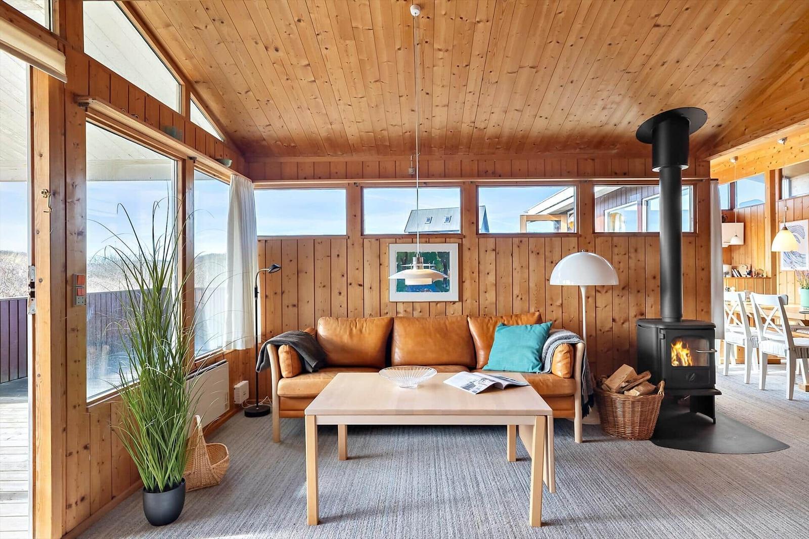 Living room with wood walls, sofa, stove, and large windows.