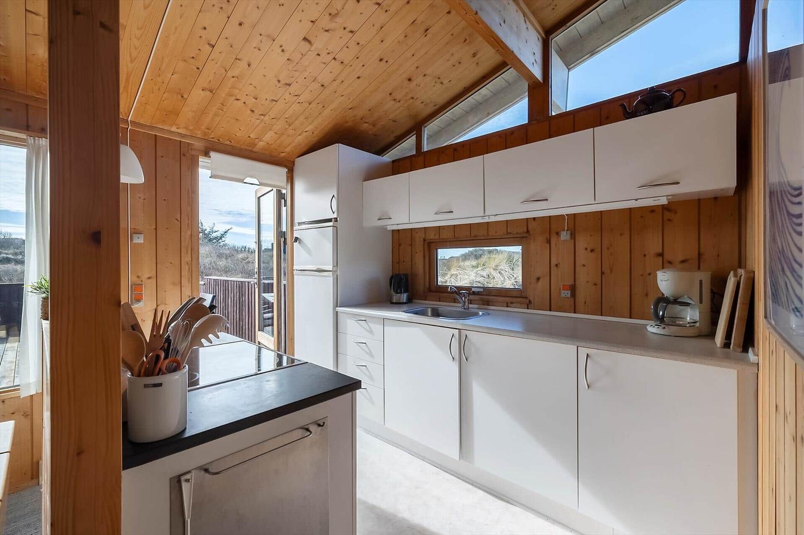 Kitchen with white cabinets, wooden walls, and windows to the balcony.
