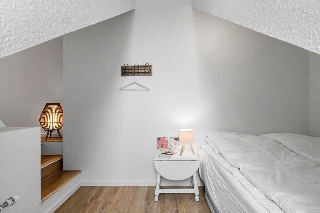 Bedroom with sloped ceiling, bed, nightstand, and lamp.