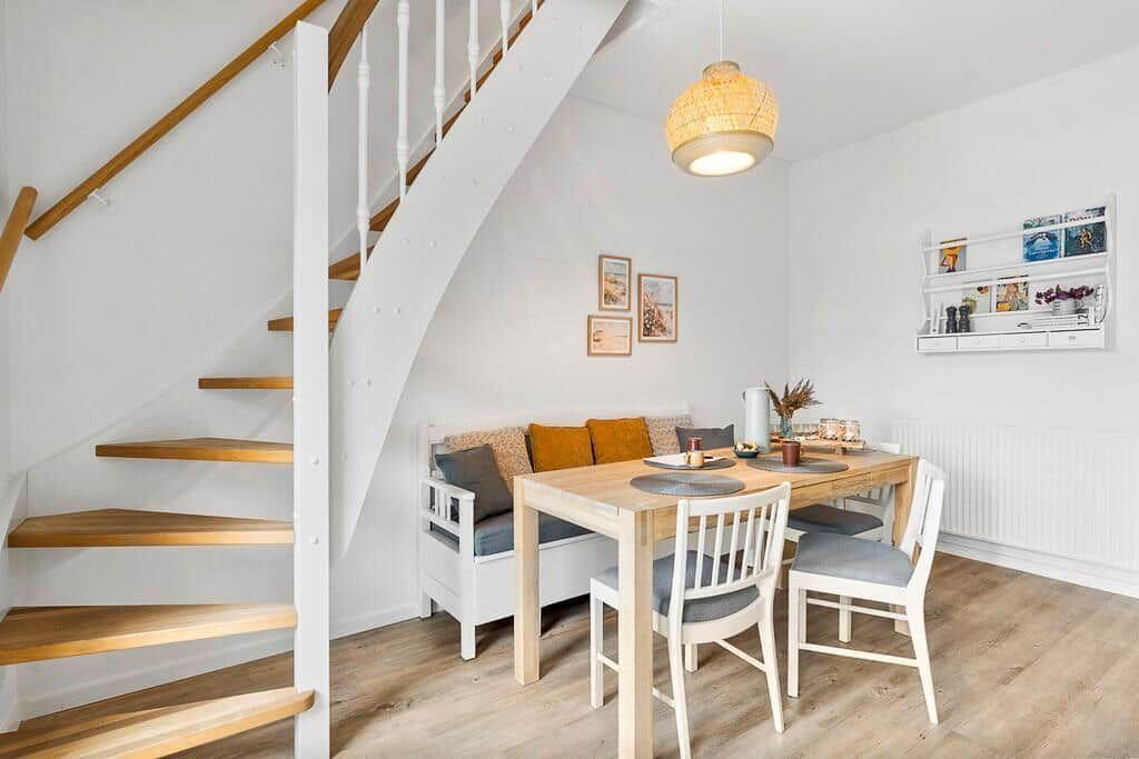 Dining area with table, chairs, and staircase. Wall shelf and pendant light visible.