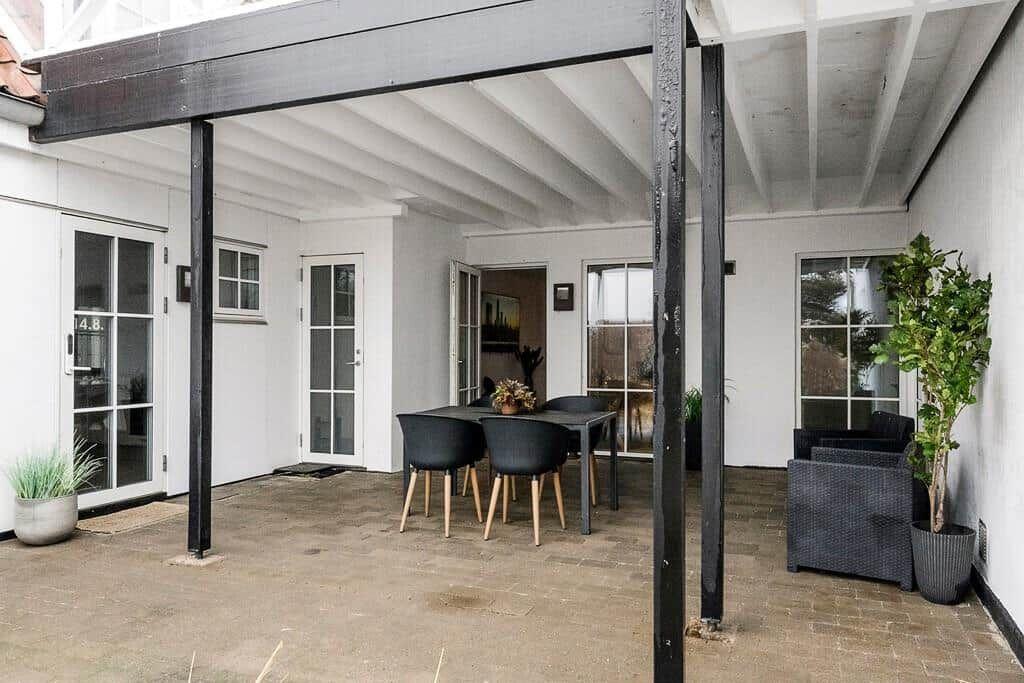 Terrace with table, chairs, and plants under wooden structure.