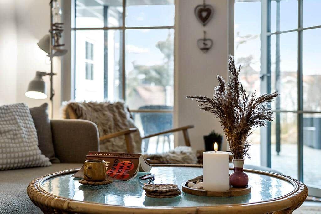 Round table with candle, dried plant, and book in living room with seating.