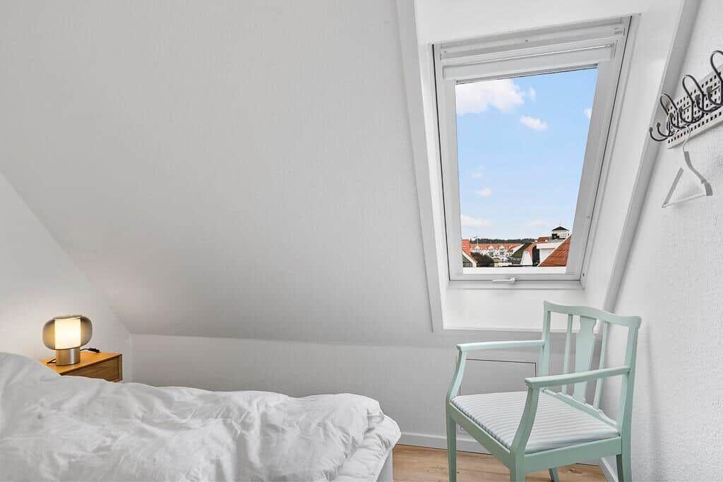 Bedroom with skylight, view of rooftops and blue sky. Wooden floor, bed, chair, and nightstand.