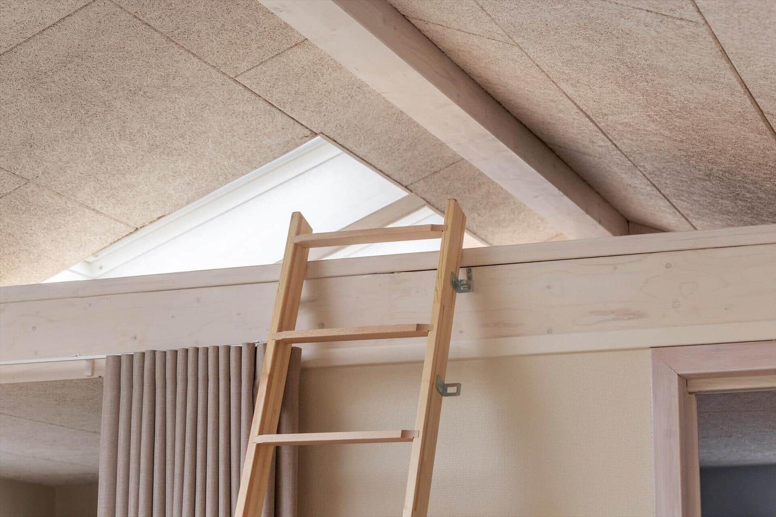Holzleiter führt zu einer Dachbodenwohnung mit Dachschräge und Fenster.