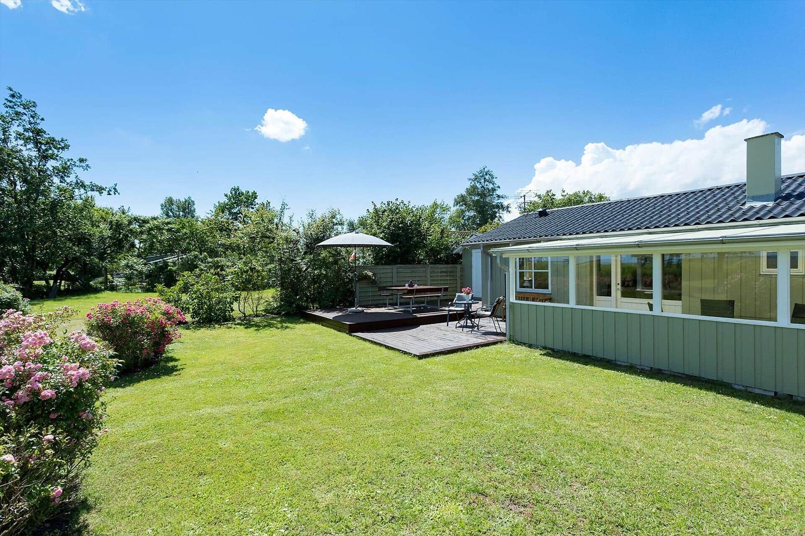 Haus mit Garten, Terrasse und Sonnenschirm. Grünfläche und Blumenbeete.