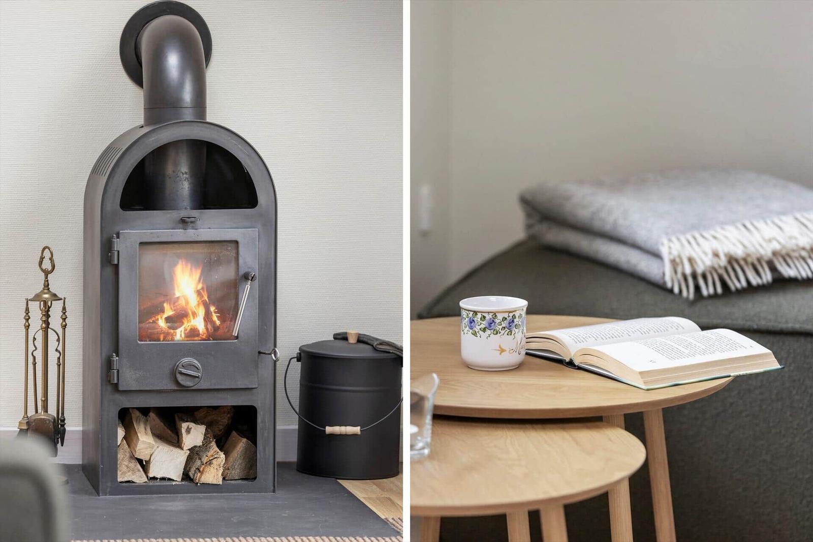 Kaminofen mit Holzstapel und Tisch mit Buch und Tasse.