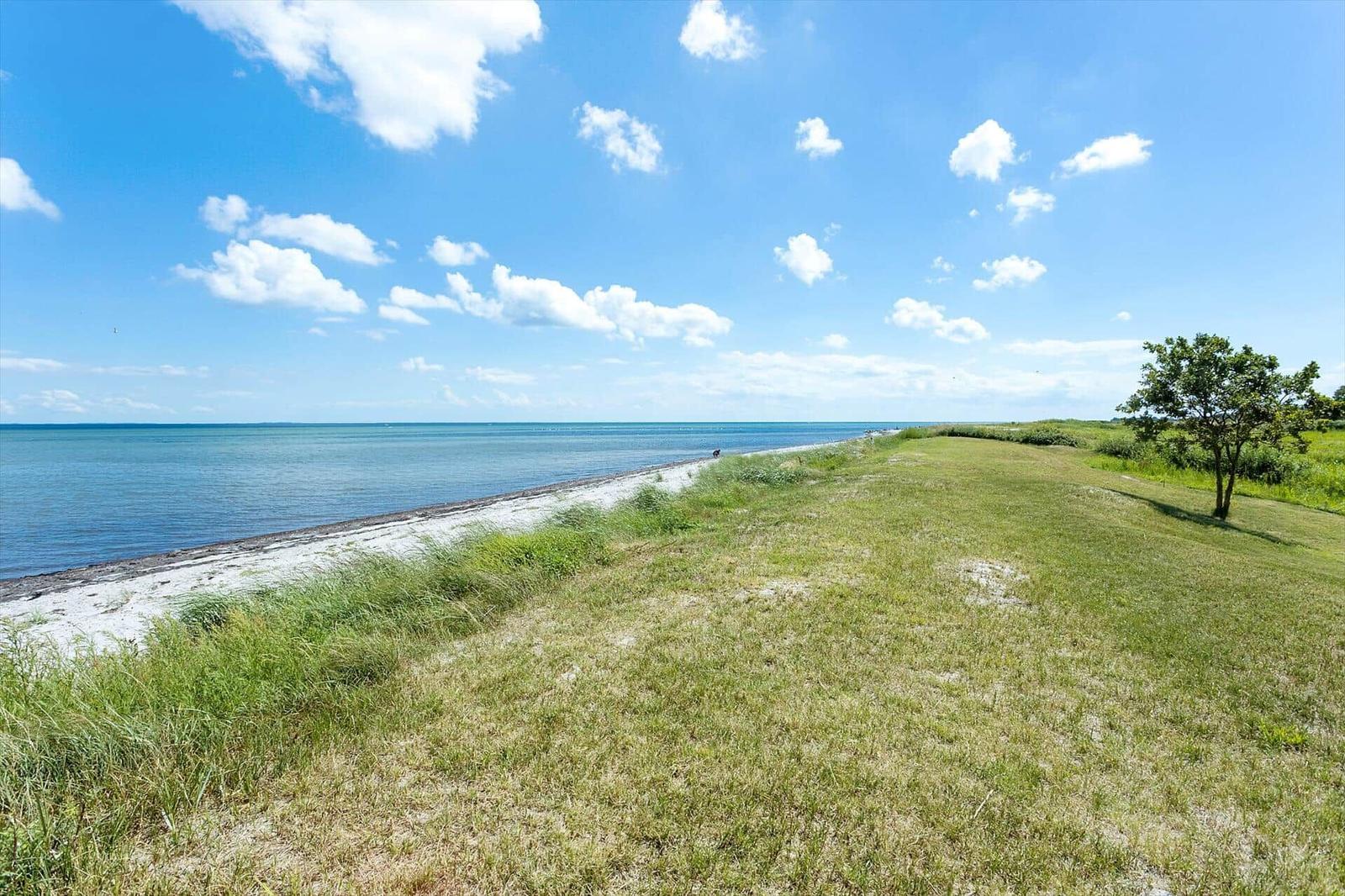Weiterer Blick auf den Strand mit Grasland und blauem Himmel mit weißen Wolken.