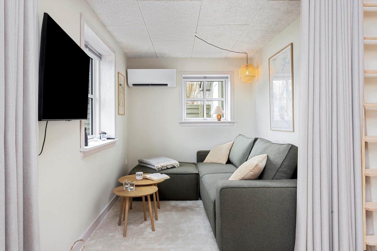 Ein Wohnzimmer mit Sofa, Fernseher und zwei Fenstern.