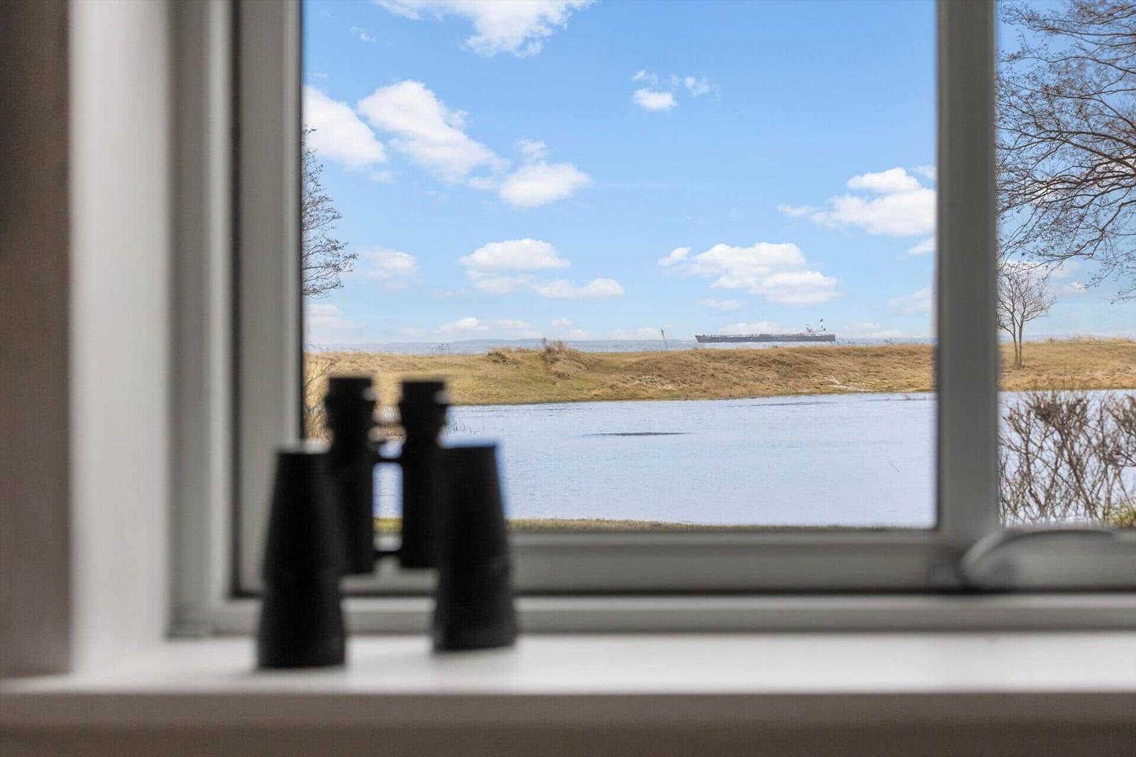 Durch das Fenster blickt man auf einen Fluss und eine Schiffsluke im Hintergrund.