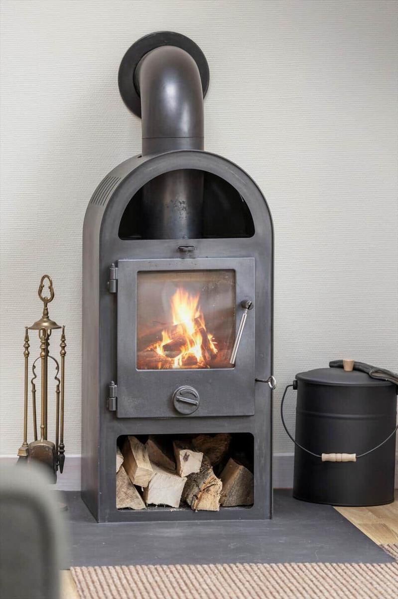 Holzofen mit brennendem Feuer und Holzstapel darunter.