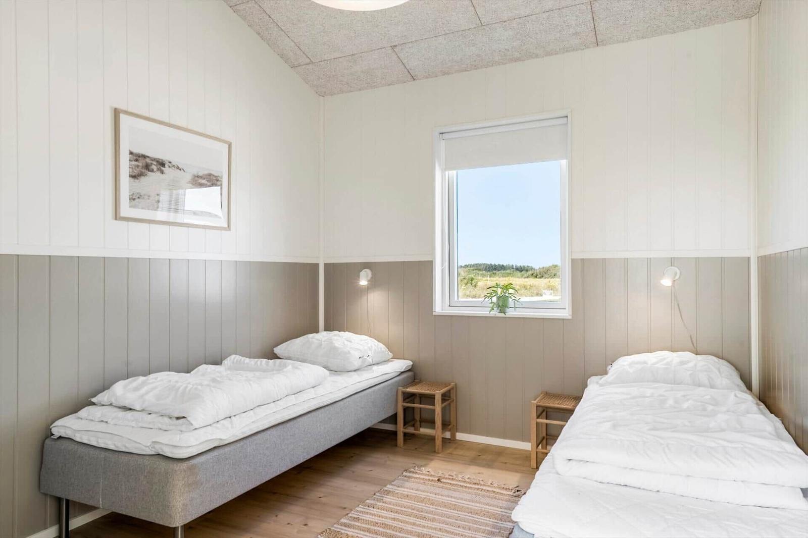 Zwei Betten mit weißen Bettwäschen, Holzfußboden und Fenster mit Blick auf Landschaft.
