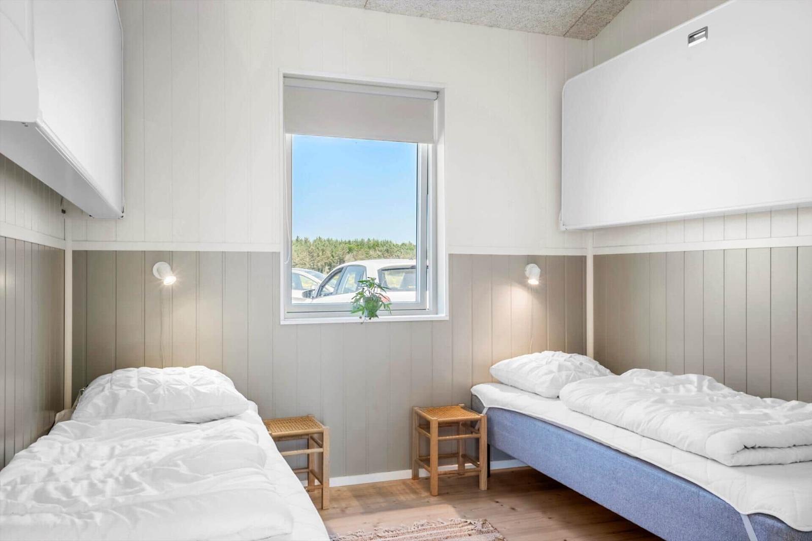 Zwei Betten mit weißen Laken, Holzstühle und Fenster mit Blick auf Parkplatz.