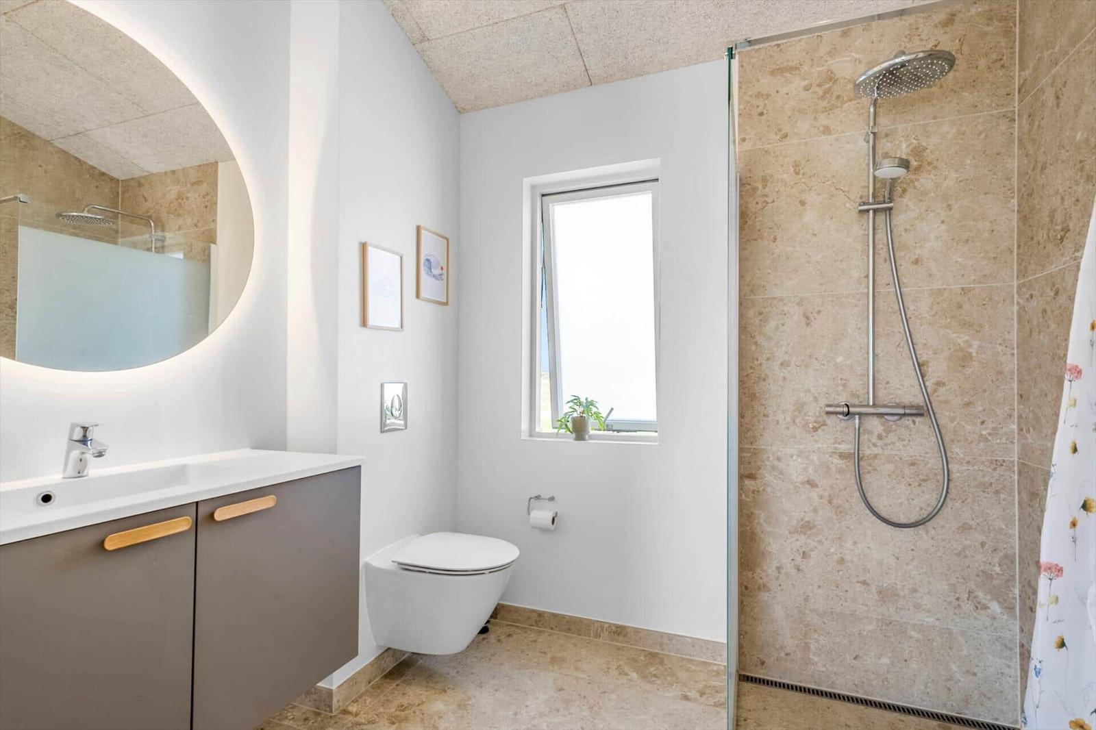 Badezimmer mit Dusche, Waschbecken und Toilette. Fenster mit Pflanze.
