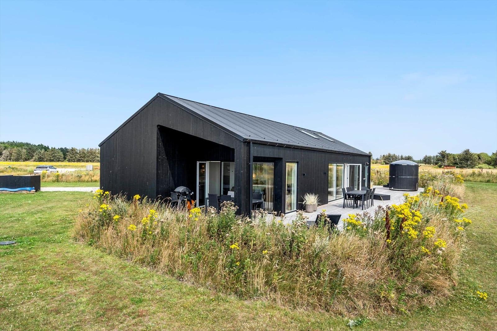 Moderne schwarze Hütte mit Terrasse, Grill und Außensitzgelegenheit in ländlicher Umgebung.