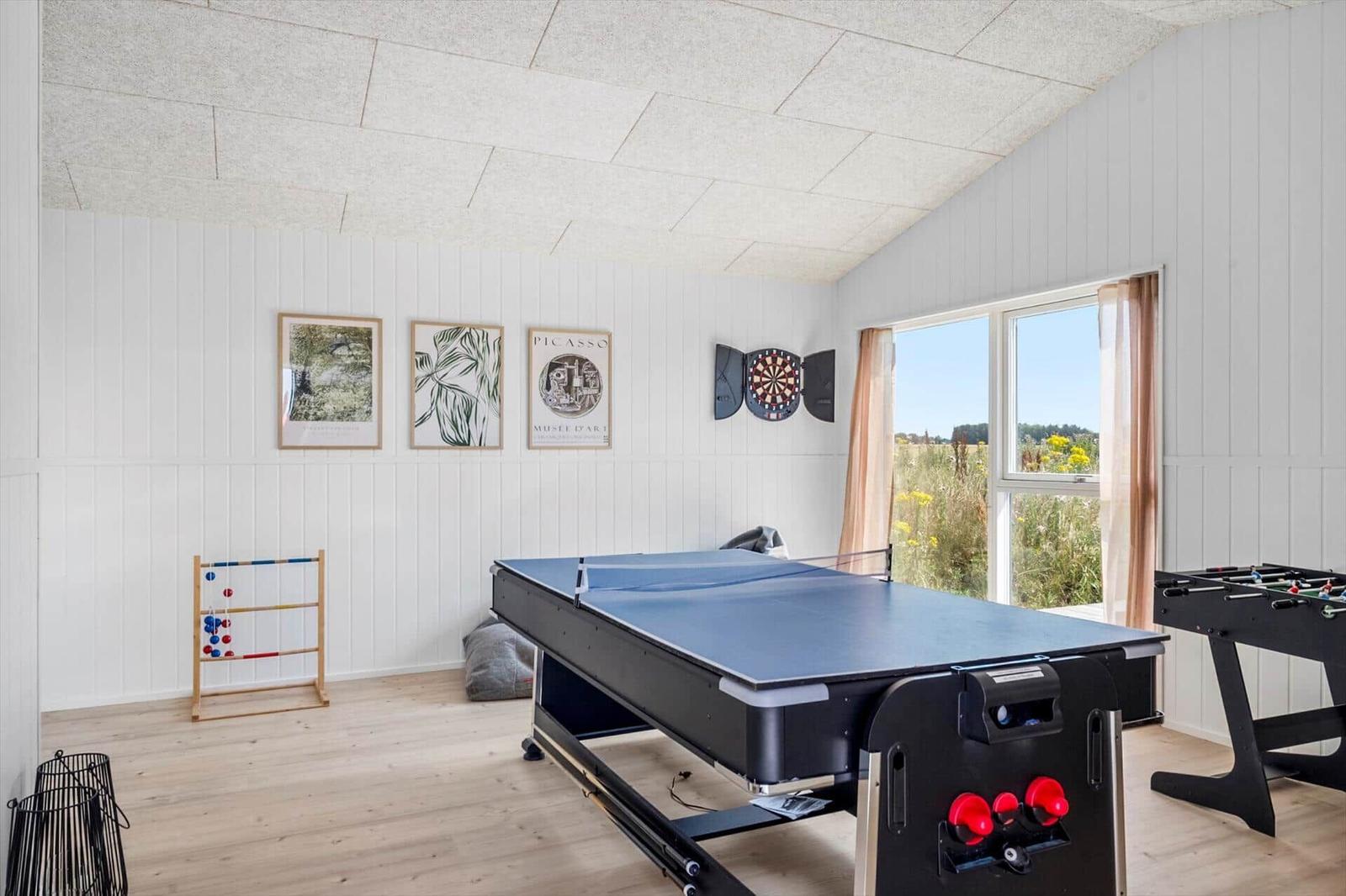 Raum mit Tischtennisplatte, Dart und Foosball. Fenster mit Blick auf Feld.