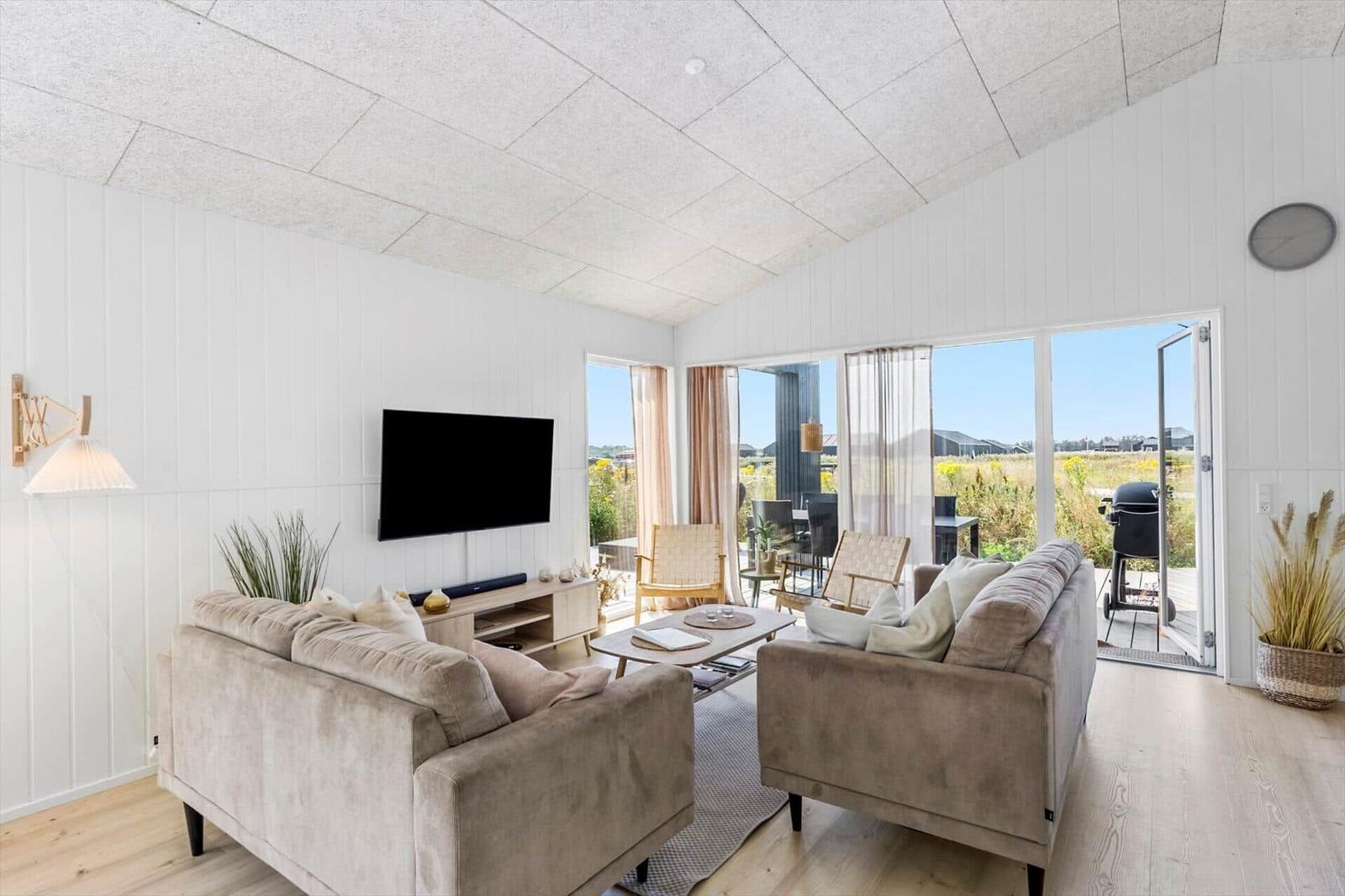Wohnzimmer mit Sofa, Fernseher und Blick auf Terrasse.