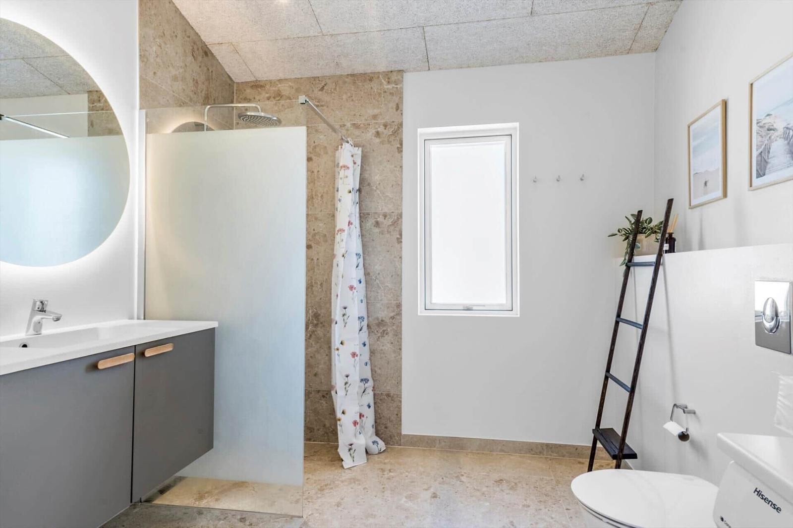 Badezimmer mit Dusche, Waschbecken und Toilette. Fenster, Spiegel und Holzstufen.