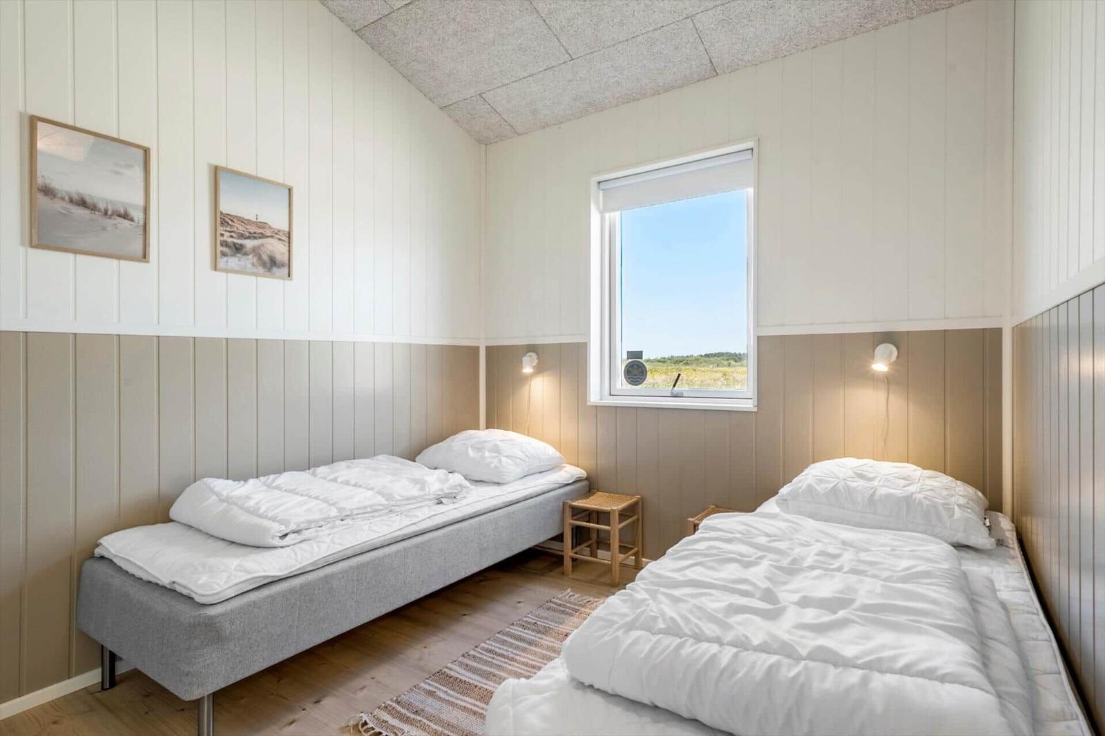 Zwei Betten mit weißen Decken, Fenster mit Blick auf Feld, Wandbilder und Holzboden.