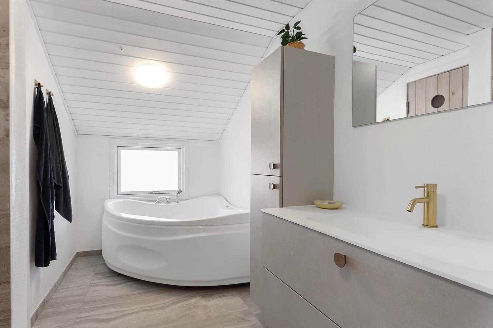 Bathroom with bathtub, sink, and mirror. Skylight window and modern fixtures.