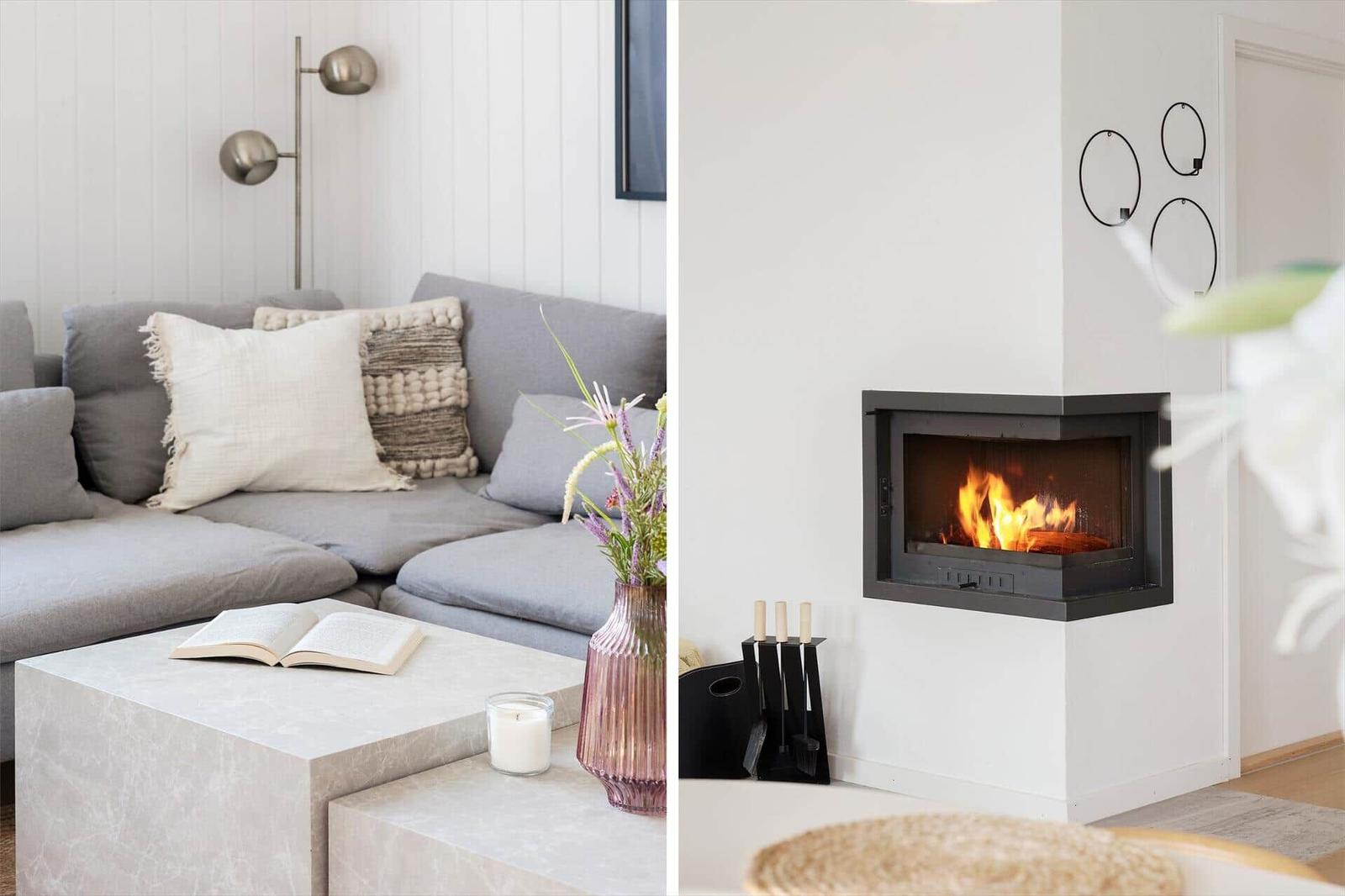 Gray sofa with cushions and table with flowers. Fireplace with burning fire on the wall.