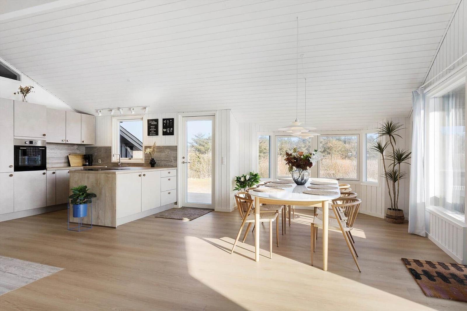 Kitchen and dining area with wooden floor, white walls, and large windows.