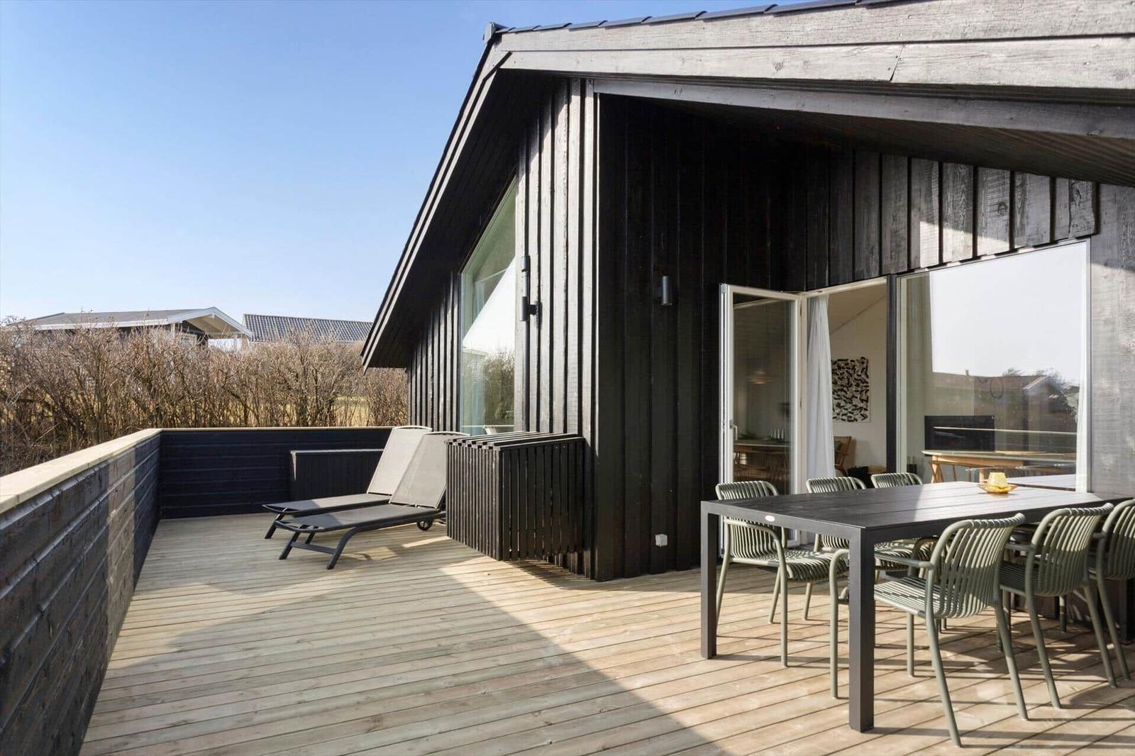 Deck with table, chairs, and loungers in front of a modern wooden house.