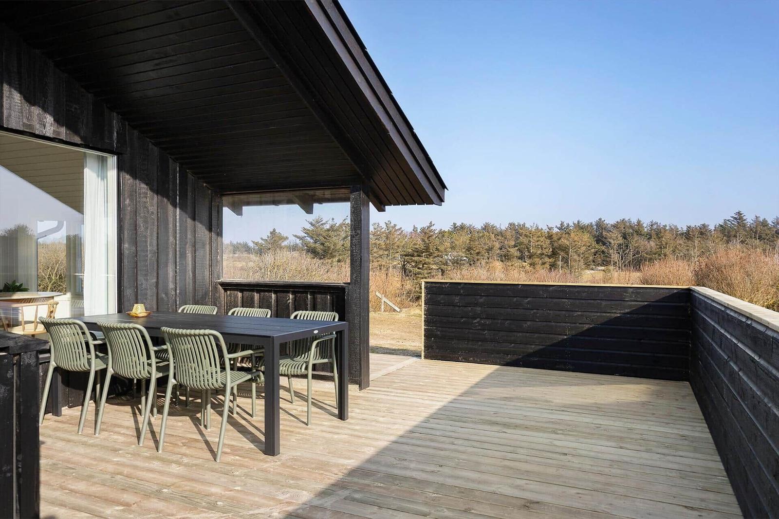 Deck with table and chairs, view of forest and sky.
