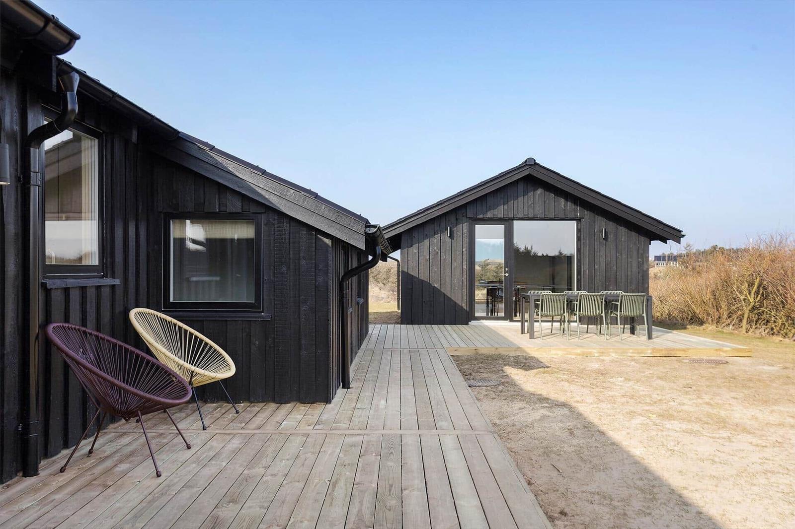 Two black wooden houses with terrace and outdoor seating.
